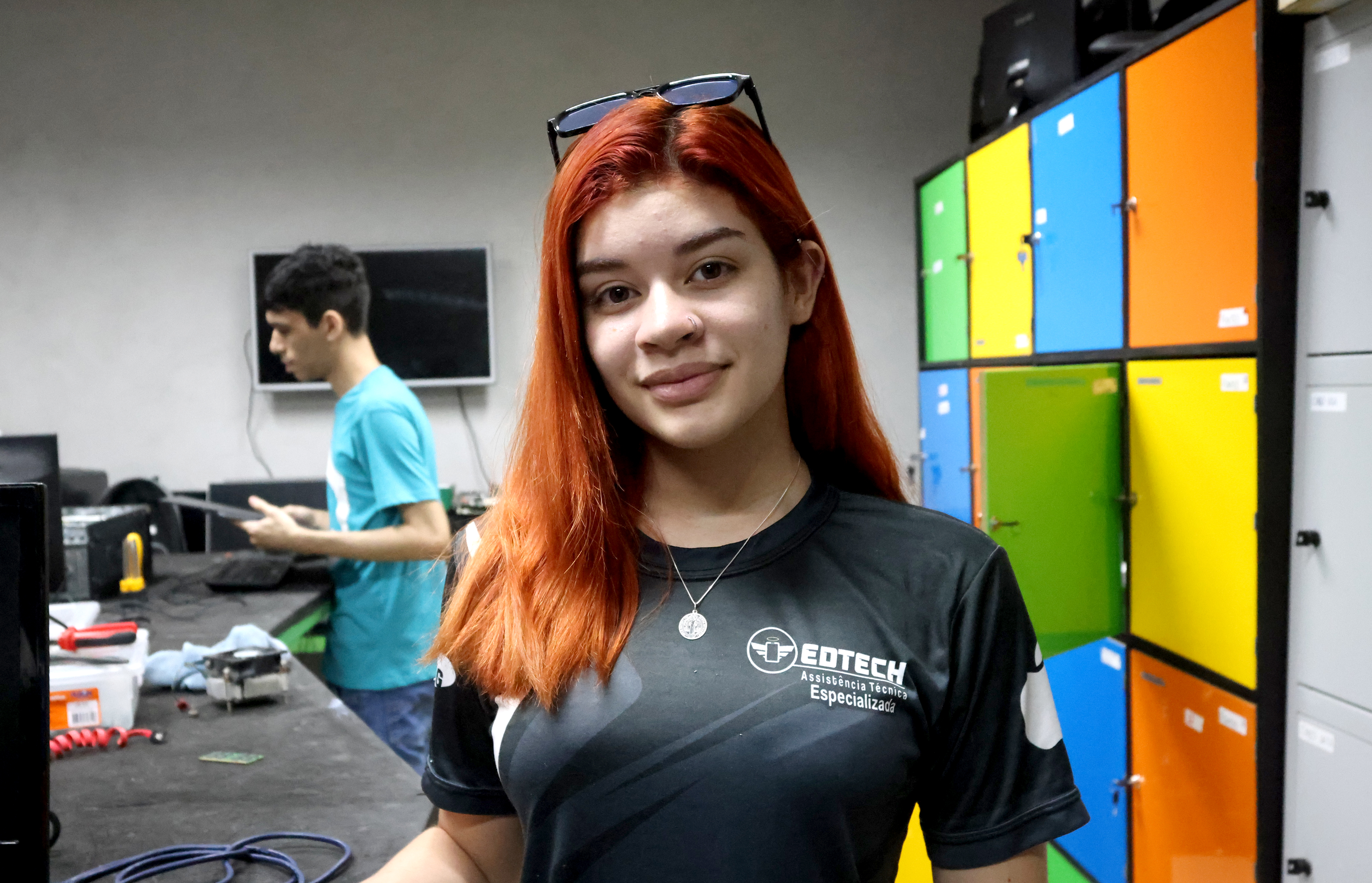 Fernanda posa para a foto, ela é uma mulher morena de cabelo ruivo e veste uma camiseta preta